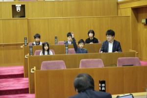 こども議会体験会でこども（3人目）が議員席で手を挙げている写真