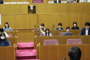 こども議会体験会でこども（4人目）が議員席で手を挙げている写真