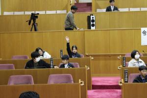 こども議会体験会でこども（9人目）が議員席で手を挙げている写真